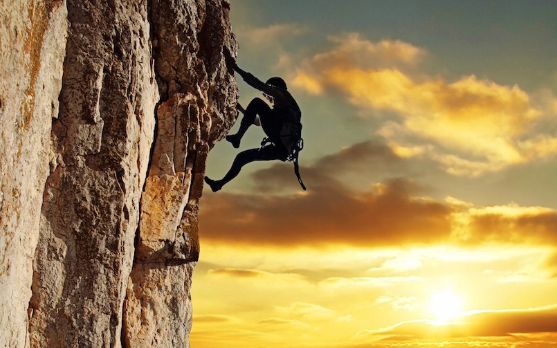 man rock climbing with setting sun in the background