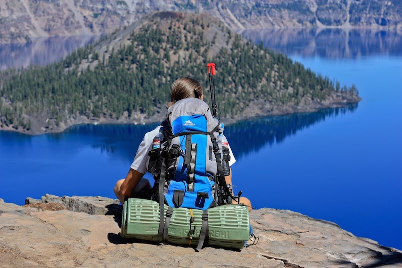 woman sitting on cliff overlooking a lake with a backpack