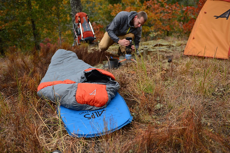 man setting up campsite and sleeping bag on the ground