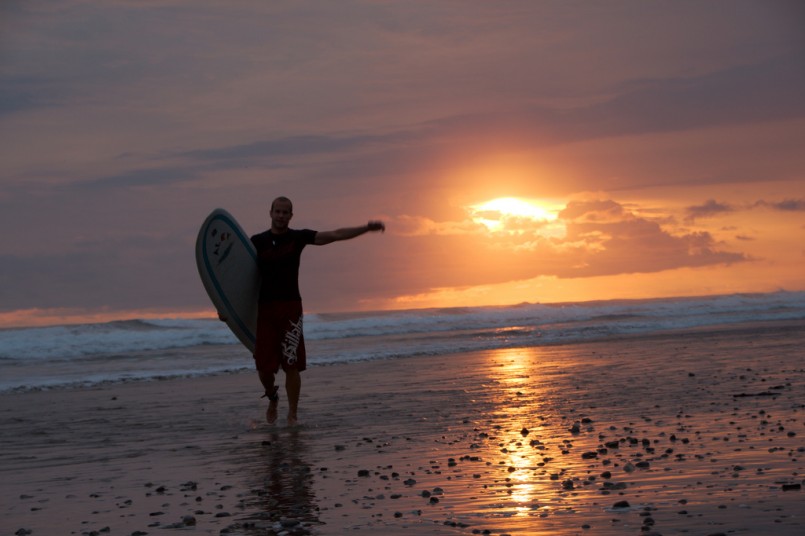man with surfboard in the setting sun