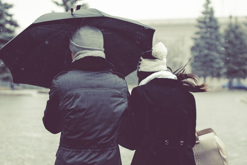 couple walking in snow with coats and umbrella