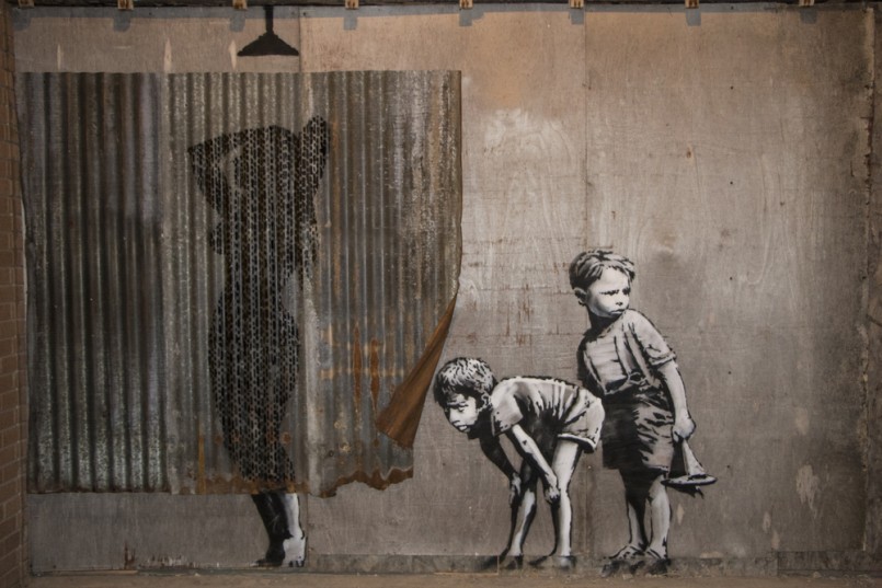 Dismaland, Banksy inpired theme park, Weston-Super-Mare, Somerset. A stencil mural by Banksy depicting boys spying on a woman having a shower
