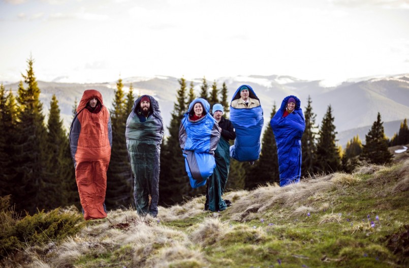 cheering group of hikers jumping in sleeping bags outdoors in mountains during the sunset