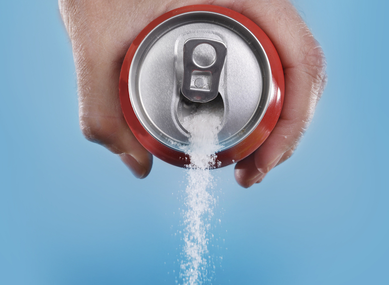 hand holding soda can pouring a crazy amount of sugar in metaphor of sugar content of a refresh drink isolated on blue background in healthy nutrition diet and sweet addiction concept